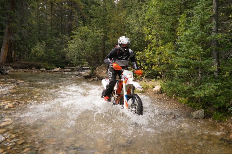 A KTM dirt bike rider crossing a creek in the forest